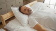 © Krakenimages.com - Middle-aged hispanic man resting in bed in a serene bedroom interior with white sheets and wooden furniture.