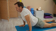 © Krakenimages.com - Man doing yoga on mat in wellness center with wooden screen candles and pillows in background.