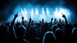 © altitudevisual - Silhouettes of concert audience with raised hands in music festival setting with bright stage lights and smoke