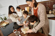 © LIGHTFIELD STUDIOS - A joyful family blends ingredients while children eagerly participate in holiday baking in their kitchen.