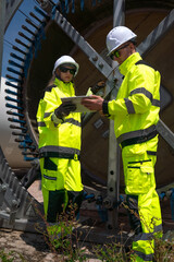 Maintenance engineer team standing at windmills at wind turbine farm. Skill people working outdoors at alternative renewable energy wind power station. Sustainable clean energy technology. Ecology