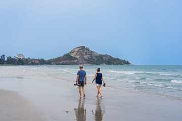 Back view of senior lovers walking together on beach. Portrait elderly couple while walking along the beach, concept of senior lifestyle, travel, relaxing in nature. Family walk on coastline at beach.