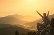 © arrowsmith2 - A hiker with a backpack raises his hand proudly for conquering a mountain peak. Traveler sits with his arms outstretched to convey success and freedom atop a misty high mountain