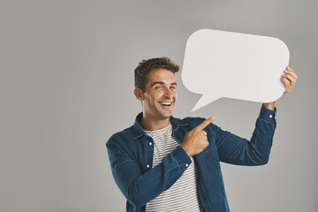 Speech bubble, man and pointing with portrait, poster or guy on gray studio background. Person, mockup space or model with social media, communication or blank billboard with branding placard or chat