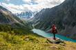 © Павел Чигирь - A tourist girl stands on a stone overlooking the beautiful mountains and Lake Shavlinskoye. Altai. Siberia