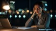 © Chayan - A woman looks stressed while working late at her desk, surrounded by city lights, depicting the challenges of balancing work and personal life.