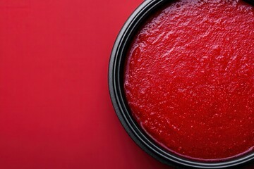 A vibrant red sauce in a black dish against a bold red background, showcasing a smooth, glossy texture perfect for various culinary uses.