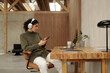 © Clique Images - Architect wearing headphones, engaging with smartphone while sitting at desk in modern office space