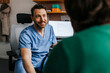 © Maskot - Smiling medical professional in scrubs consoling patient while sitting on chair in examination room