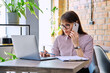 © Valerii Honcharuk - Portrait off middle-aged business woman working with laptop, talking on phone, sitting at desk