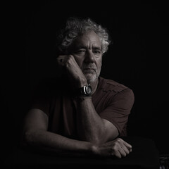 Low key black and white portrait of an attractive older Caucasian man with grey hair and beard. Looking at camera with serious or pensive expression.  