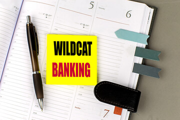 Wildcat banking concept with text on a yellow sticky note, open planner, pen, and bookmarks,