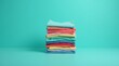 © Alex Pios - A neatly folded stack of colorful clothes stands against a vibrant turquoise backdrop, radiating joy and tidiness with each layer of bright fabric.