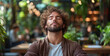 © sommersby - A man with curly hair sits calmly in a café surrounded by greenery, practicing mindfulness and enjoying a quiet moment in a vibrant atmosphere