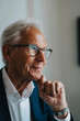 © Maskot - Smiling senior businessman with hand on chin wearing eyeglasses in office