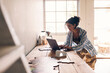 © Maskot - Female designer working on laptop while leaning at table in workshop