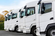 © Kyryl Gorlov - Fleet of new modern electric hybrid hydrogen or diesel white trucks parked in line row outdoors. Cargo freight industrial transportation logistics service. Commercial vehicles maintenance insurance