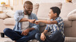 © Prostock-studio - Father And Son Connection. Cheerful Black Preteen Boy Fist Bumping With His Dad At Home, Enjoying Spending Time Together