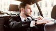 © Prostock-studio - Young handsome bearded businessman in suit sitting in luxury car, looking out of window at city