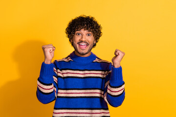 Photo portrait of handsome young guy winning raise fists dressed stylish blue striped garment isolated on yellow color background