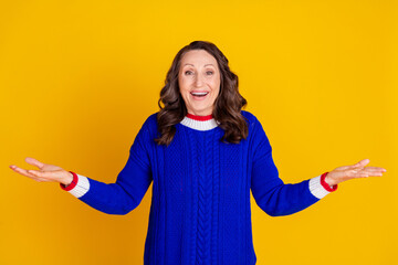 Photo of attractive retired woman compare hold excited empty space dressed stylish blue knitted clothes isolated on yellow color background