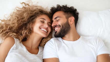 A happy couple lies together on a white bed, smiling and enjoying a joyful moment of togetherness, emphasizing love, warmth, and comforting happiness indoors.