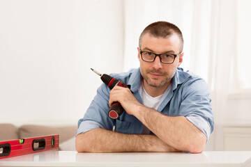 Aufkleber - Furniture Assembly. Man Holding Electric Drill Fixing Table Using Carpentry Tools Sitting Looking At Camera At Home.