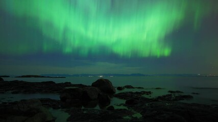 Wall Mural - Aurora Borealis shining at night and reflecting in the ocean water. Timelapse