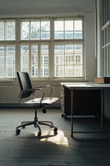 Poster - A black office chair sits in front of a desk with a window in the background. The chair is empty and the desk is bare, with only a few papers on it. The room is dimly lit