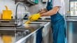 © Jiraphat - A person wearing yellow gloves cleans a kitchen sink with a brush, showcasing a tidy and well-maintained cooking space.