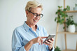 © CoveRipple - Elderly woman with smartphone, blue shirt, cheerful expression