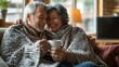 © Oulaphone - A cozy, heartwarming moment between an elderly couple sharing laughter while wrapped in blankets and enjoying a drink together.