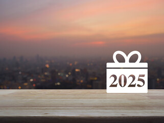 Wall Mural - Gift box happy new year 2025 flat icon on wooden table over blur of cityscape on warm light sundown, Business shop online concept