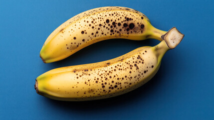 Wall Mural - Two ripe bananas with brown spots on a blue background, showcasing the natural ripening process and texture of the fruit.