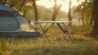 © Suphawan - Compact camping table with minimalist style, set up by a tent on grass, lightweight and easy to transport.