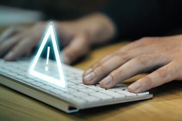 Close up and side view of man hand using computer keyboard with glowing attention sign on blurry background. Important notice and alert concept.