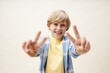 © Seventyfour - Portrait of preteen boy in pastel color clothes smiling at camera while showing V sign with both hands against neutral background in studio, copy space