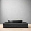 © sergign - A contemporary black square platform with a round topper sits on a wooden surface, integrating sophistication and modern design styles with earthy elements.