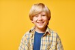 © Seventyfour - Portrait shot of cute smiling boy wearing casual plaid shirt looking at camera while standing against yellow background in studio, copy space