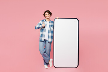 Wall Mural - Full body young happy woman she wear blue shirt white t-shirt casual clothes big huge blank screen mobile cell phone smartphone with area show thumb up isolated on plain pastel light pink background.