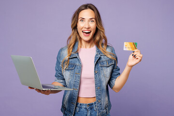 Young IT woman wear denim jacket violet top casual clothes using laptop pc computer hold credit bank card shopping online order delivery booking tour isolated on plain pastel light purple background