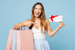 © ViDi Studio - Young woman wear casual clothes hold in hand shopping paper package bags point on gift certificate coupon voucher card for store isolated on plain blue background. Black Friday sale buy day concept.