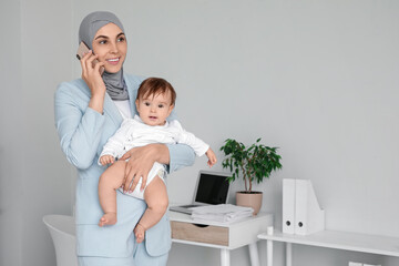 Poster - Young happy business Muslim mother in hijab with little baby talking by mobile phone at home