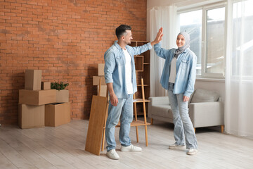 Happy Muslim couple giving each other high-five after assembling shelf unit at home