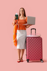 Wall Mural - Young businesswoman with laptop and travel accessories waiting for summer vacation on pink background