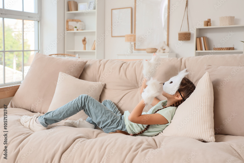 Quadrober girl in cat mask lying on sofa at home