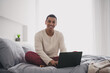 © deagreez - Full size photo of attractive young male hold netbook working dressed pajama wake up cozy day light home interior bedroom