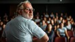 © JoxyAimages - A bearded man with glasses, wearing a striped shirt, looks back over his shoulder towards a seated audience, suggesting an academic or lecture setting.