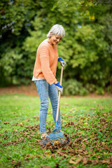 Senior woman raking leaves in an autumn garden