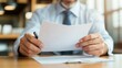 © Lens Legacy - A close-up image of a businessman in professional attire thoroughly reading a formal document in an office, emphasizing careful analysis and diligence.